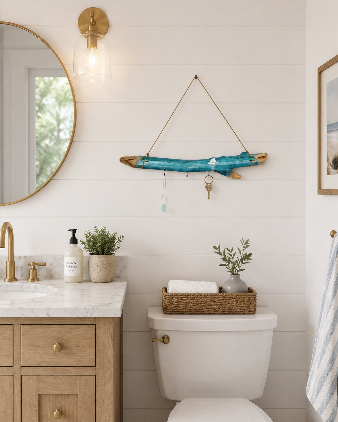 Driftwood wall hanger with teal resin sailboat painting and three hooks, displayed on a white shiplap wall above a bathroom vanity