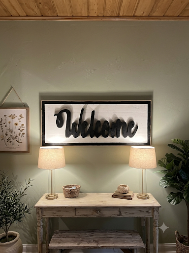 Rustic welcome sign with black frame styled above an entryway console with lamps and greenery