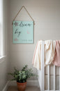 Dream Big Little One sign hanging in soft dreamy nursery with white crib and blush linen accents